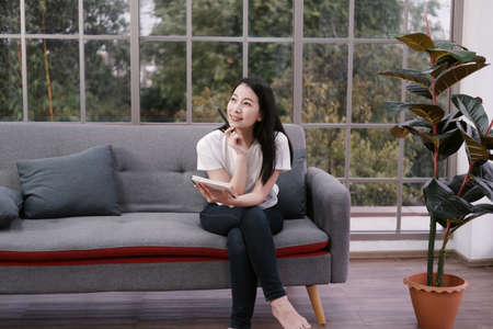 Smiling Asian businesswoman in white shirt is planning and writing on notebook for business planner...