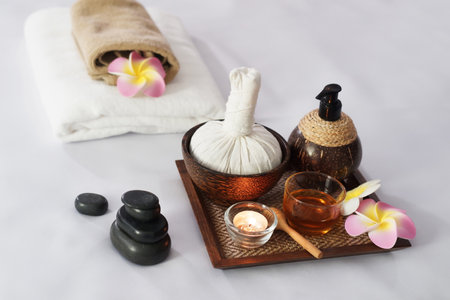 Hot compress herbs, Atmosphere candle, honey glass on Herbals tray for therapy massage. Natural black stone and Plumeria flowers decorate on bed at alternative medicine healing spa Center in Thailand.の写真素材