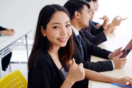 Smiling Asian business woman is thumbs up for good seminar course and marketing knowledge planning in classroom with businesspeople and partnership in meeting room.の写真素材