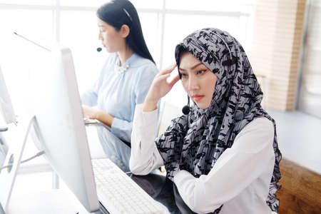 Serious asian call center muslim woman or secretary operator with headset and a microphone is having trouble and have a headache for consultant to customers. Technician Support staff at official.の写真素材