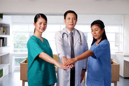 Asian chief physician man is holding hand with surgeon doctor women wears blue and green surgical gown together. Smiling Medical team in meeting room at hospital.の写真素材