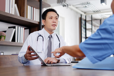 Asian chief physician man is meeting with surgeon doctor woman wears blue surgical gown. Medical team are talking and researching with laptop for treatment of patients in meeting room at hospital.の写真素材