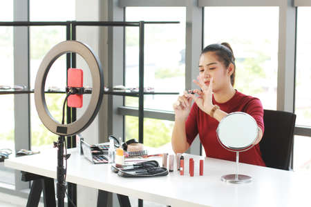 Beautiful Asian woman blogger recording on red smartphone for make up tutorial video in Cosmetics Vlog website. Youtber and Marketing in social media concept.の写真素材