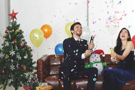 Sweet couple Love smile and spending Romantic with confetti Paper fireworks in christmas time and celebrating new year eve, valentine day with colorful balloon on brown sofa in living roomの写真素材