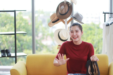 Smiling Beautiful Asian woman blogger sitting on yellow sofa and recording on video Dslr Camera for selling shoes online shopping on website. Marketing in social media concept.の写真素材
