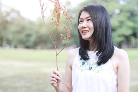 Beautiful asian woman in white dress smiling and hand holding Dry twigs in natural park. Thai girl...