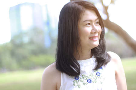Beautiful asian woman in white dress relax and smiling in natural park. Thai girl or Chinese Girl enjoy on holiday with sunlight in gardenの写真素材