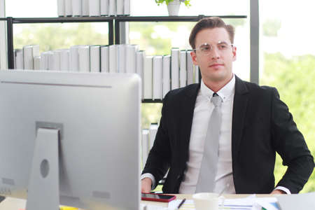 Handsome businessman in black suit wear eyeglasses happy and working computer desk in Office