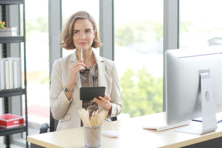 Businesswoman in white suit hand holding pen and tablet for writing and thinking in job at workspace in officeの写真素材