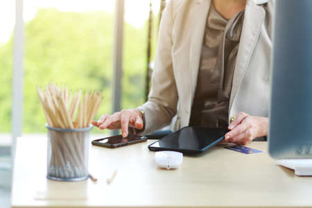 Businesswoman in white suit working with computer, laptop, smartphone and pencils in box on desk in modern officeの写真素材