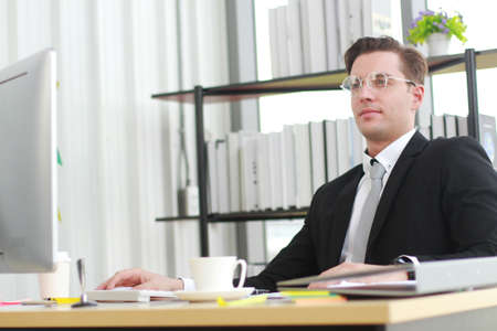 Handsome businessman in black suit wear eyeglasses and happy working with computer, notebook, laptop and smartphone on desk in modern officeの写真素材