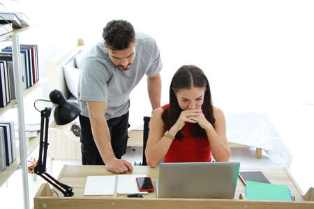 Serious Caucasian Couple love working from home with laptop for online in social media technology on computer desk in bedroom. Lifestyle and relationship of married life on holiday Concept.の写真素材