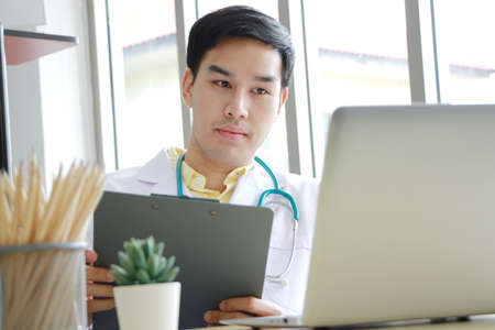 Smiling Professional Asian Psychiatrist man is studying and researching for treatment Mental health patients at Medical Research Library. Doctor clinic office concept.の写真素材