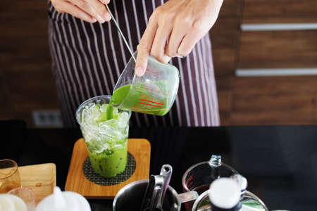 Closed up on hand of Asian barista young man pouring fresh milk is mixing with green tea in a plastic glass of iced greentea  for according to order at counter bar in the morning at modern cafe.の写真素材