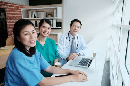Smiling Asian chief physician man is meeting and brainstorming with surgeon doctor women wears blue...