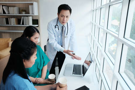 Serious Asian chief physician man is meeting and brainstorming with surgeon doctor women wears blue...