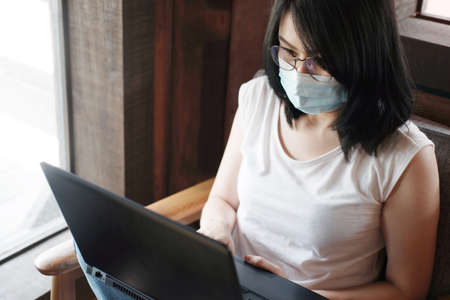Asian young woman is wearing mask prevent for civid-19 and online working with laptop in office. She...
