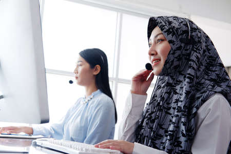 Smiling asian Muslim women is call center or secretary operator is wearing a headset and a microphone for consultant to customers. Technician Support staff for help resolve technical issues.の写真素材