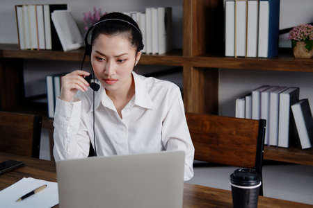 Asian woman is call center or secretary operator is wearing a headset and a microphone for...
