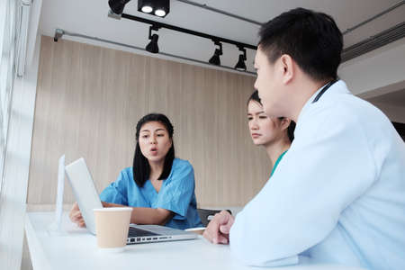Serious Asian chief physician man is meeting and brainstorming with surgeon doctor women wears blue...