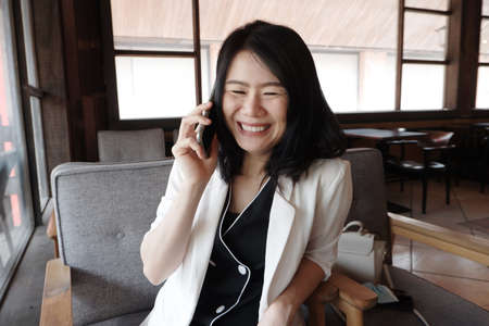 Smiling Asian businesswoman is is calling with smartphone online working in social media at...
