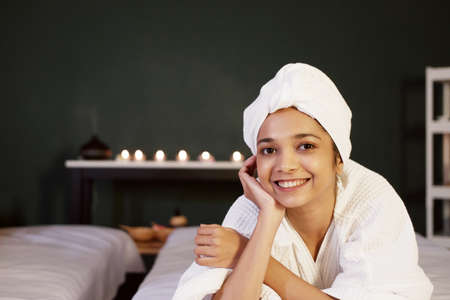 Smiling Asian woman in white headscarf and bath towel lie down on bed preparing for massage therapy at alternative medicine healing spa Center in Thailandの写真素材