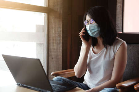 Asian woman is wearing mask for prevent covid-19 and calling on smartphone. Businesswoman is online...