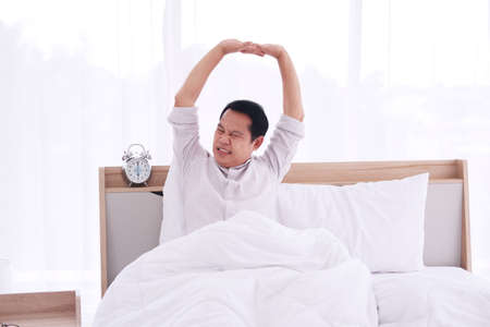 Asian man is Stretching lazily after waking up or snapping on bed in bedroomの写真素材