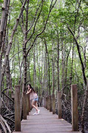 Pretty Asain girl is smiling and standing on wooden bridge in the tropical mangrove forest at Thailand.の写真素材