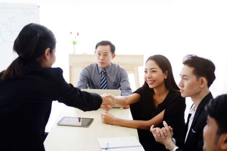 Smiling successful Asian businesswomen in black suit is shaking hand with partnership for a big project in meeting room at office. Business and marketing concept.の写真素材