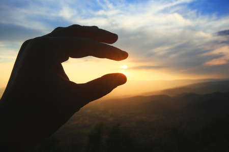 Beautiful silhouette hand holding on sun and sunset on the mountain. Power and hope Concept.