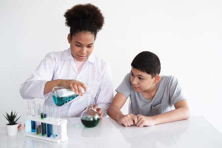 Smiling African black woman is studing and testing for chemical and science. She is experimenting and teaching Caucasian studen boy at laboratory Lab of school. Education and knowledge concept.の写真素材