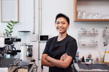 Asian Young barista woman is wearing apron standing and Smiling for happy at counter bar in cafe. Start up for Coffee shop and cafe business owner concept.の写真素材