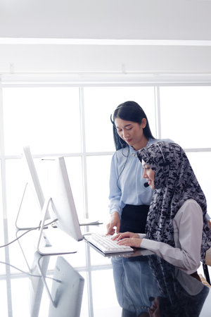 Smling asian and muslim women are colleagues and call center or secretary operator with headset and a microphone together. They are Consulting to solve problems about customers at office.の写真素材