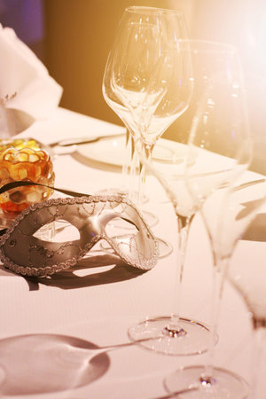 Silver mask, wine glass and  yellow candle decoration on white tablecloth with golden light in Christmas  and new year party.の写真素材