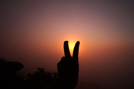 Beautiful silhouette of Female hand raised up with two lifted fingers in natural sunrise and sunset for encourage herselfの写真素材