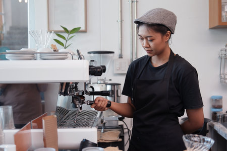 Smiling Asian Young barista woman is wearing apron and brewing coffee with machine for customers order in cafe and coffee shop. Start up small cafe business and technology Concept.の写真素材