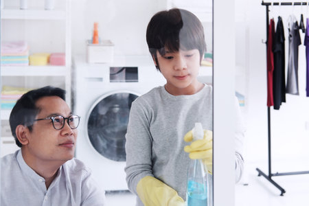 Smiling Asian father and little boy child is enjoying for cleaning and Wiping the glass together in Laundry room. Family time on holiday concept.の写真素材