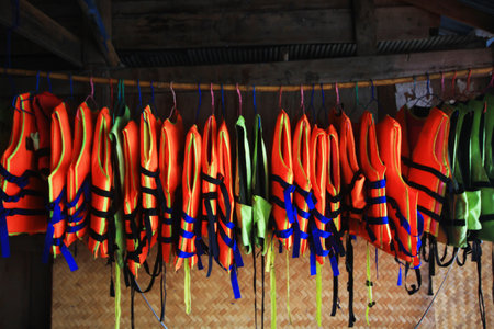 Orange life vest jackets hanging on rack outdoor for safety and protection while using in as swimming at the sea.の写真素材