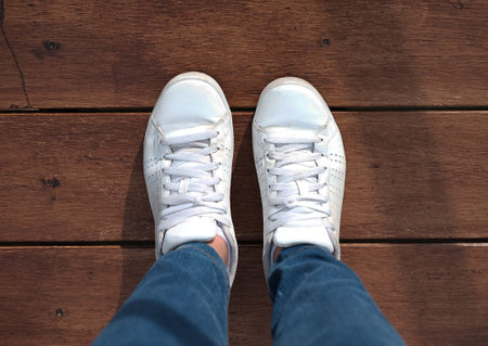 Top view of white sneakers and Blue jeans on woman legs on wood floor background