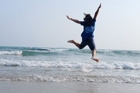 Happiness of Asian woman is jumping on sky with sea and wave on the sand beach in natural sunset. Freedom lonely life on vacationの写真素材