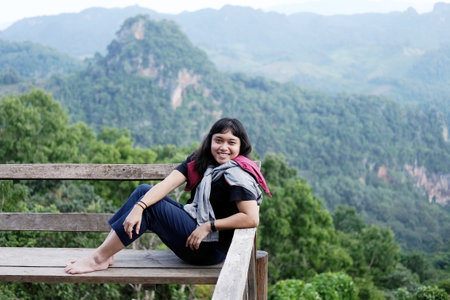 Asian woman sitting and relaxing on wooden bench on terrace for freedom journey with valley mountain and foggy in natural and travel destination in tropical rain forestの写真素材