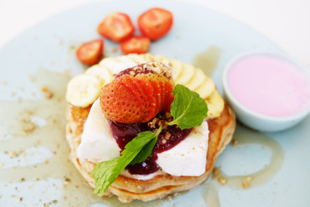 homemade pancake with fresh banana with strawberries and raspberry sauce, honey in whipped cream on...