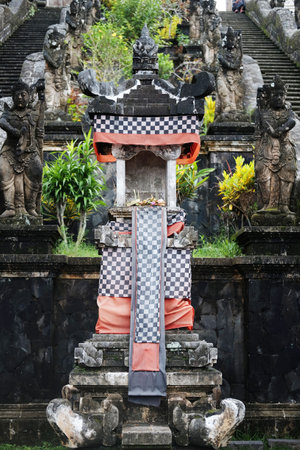 Ancient stucco statue shrine of the household god house decorated with black and white checkered fabric in Bali temple, Indonesiaの写真素材
