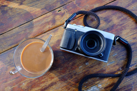 Vintage mirrorless camera and a glass cup of hot coffee on wooden table. Top viewの写真素材