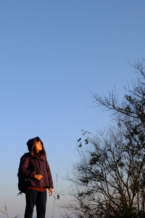 Traveler Asian woman wearing jacket and hood walking on green lawn grass and blue sky with sunrise in winter with valley mountain viewの写真素材