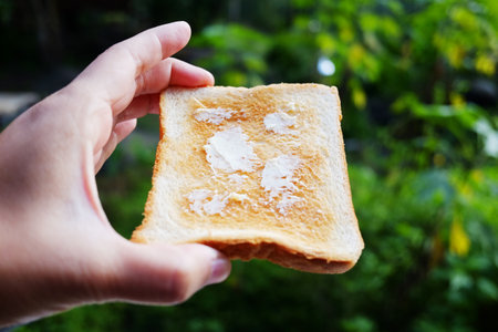 Close up hand holding buttered toast is breakfast in the morning on green natural background