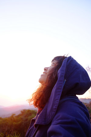 Traveler Asian woman wearing jacket and hood smiling in blooming wildflower on green lawn field with...