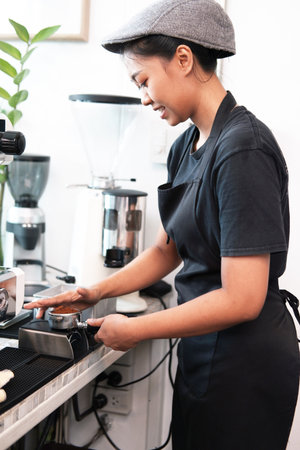 Smiling Asian young barista woman wearing apron and brewing coffee with machine for customers order in cafe and coffee shop. Start up small cafe business conceptの写真素材