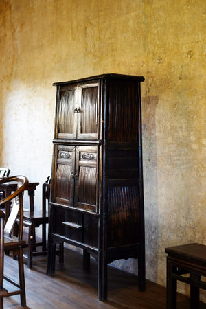 Close up antique wooden furniture of cabinet and chairs of Chinese style in vintage and rustic grunge concrete wall on wooden floor in dining room with natural sunlight in Bangkok of Thailandの写真素材